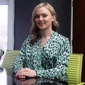 Professional headshot in which Shannon sits at a boardroom table. Her hands rest on the table top in front of her. She is looking directly at the camera.